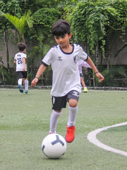 A young player dribbles along the white line of the pitch, practicing his ability to keep the ball in play and control it with precision.