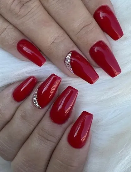 A glamorous deep red manicure on coffin nails, with a sparkling rhinestone accent on the ring finger.