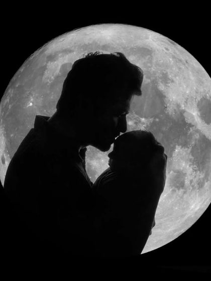 A father's love captured in silhouette, as he kisses his newborn's forehead against the backdrop of a full moon.