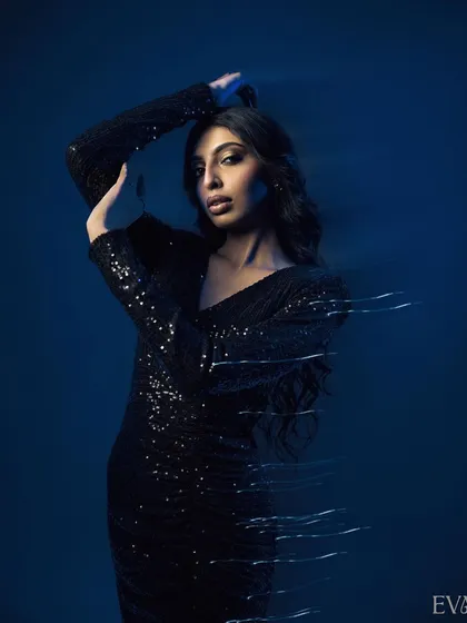 A powerful pose with the model's arms raised, enhanced by motion blur light streaks. The dark blue background makes the sequined dress and the light effects pop.