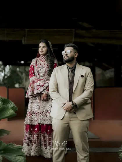 A stylish portrait of the couple, the bride in a magnificent red lehenga and the groom in a sharp beige suit.