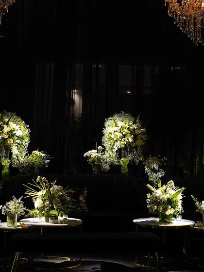 A lounge area with dark velvet sofas and multiple floral arrangements on nesting tables, all under the soft light of crystal chandeliers.