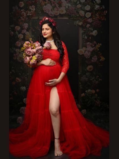 Bold, beautiful, and blooming with love. This mom-to-be in a stunning red gown holds a bouquet of flowers, set against a dark floral frame.