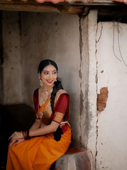 A portrait of a model seated against a rustic wall, looking away with a gentle smile. The soft lighting and traditional saree create a timeless and peaceful mood.