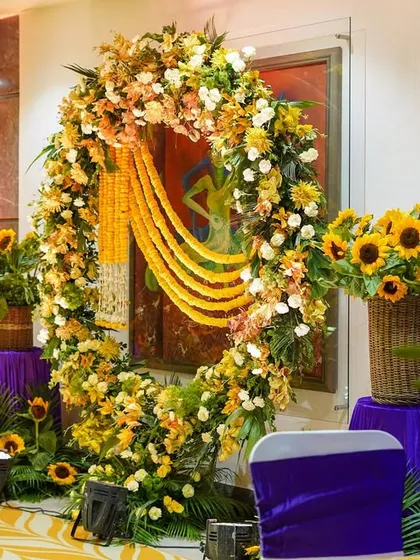 A circular floral arch created for a Haldi ceremony. This beautiful structure, made with sunflowers, white chrysanthemums, and marigold garlands, serves as a perfect frame for the couple's seating or as a photo booth.