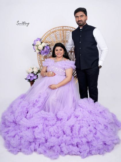 A regal portrait of a couple, with the mother-to-be seated on a peacock chair in a lavender gown. Their elegant attire and poised expressions create a sophisticated and timeless image.