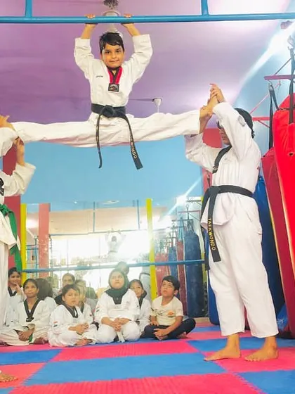 A dynamic display of flexibility and teamwork. This student performs a hanging split, supported by two of his training partners, showcasing both strength and trust.