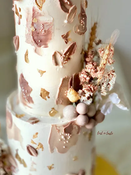 This two-tiered boho birthday cake combines textured buttercream in neutral tones with dried florals and edible chocolate spheres. It's a perfect example of rustic elegance for a stylish celebration.