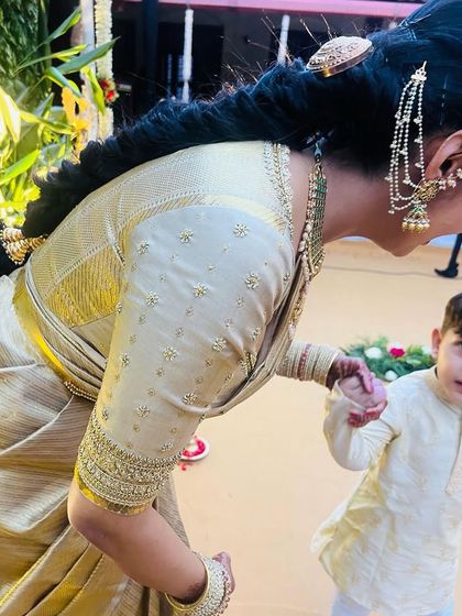 A candid moment showing the delicate embroidery on the sleeve of Neha's gold blouse, as she interacts with a little one.