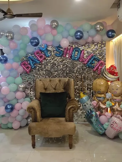 A beautiful baby shower setup for a baby girl. This design features a silver sequin wall, a pastel pink, blue, and mint balloon arch, and large foil balloons spelling 'Baby Shower' and 'It's a Girl'.