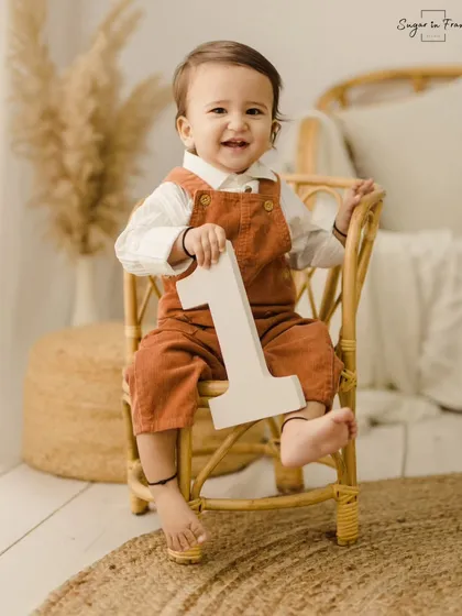 Such a happy smile for his first birthday. This little one is sitting proudly with the number '1' in our rustic, boho-themed studio setup.