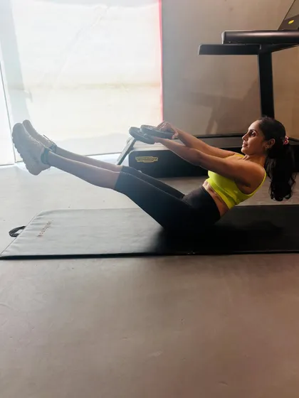 This image shows a teaser exercise using a Pilates ring, or magic circle. Squeezing the ring between my hands engages the chest and arm muscles, adding an upper-body component to this classic core-strengthening pose.