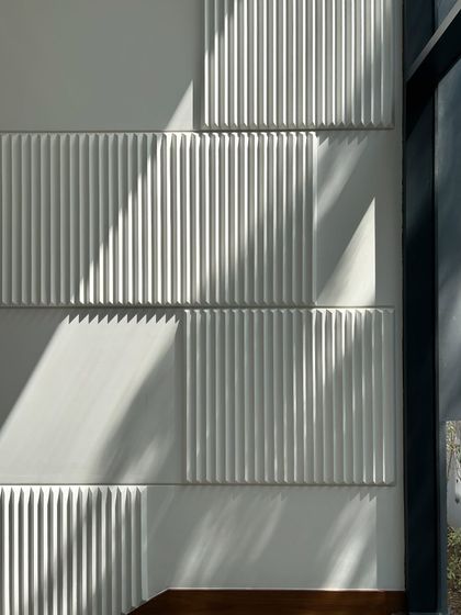 A detail of the textured wall panels alongside the Gulmohar Farmhouse staircase. The play of sunlight and shadow across the fluted surface creates a dynamic and artistic effect.