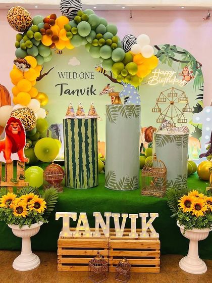 A 'Wild One' jungle theme with a touch of elegance. This setup features a green grass floor, sunflower arrangements, a wooden fence, and various animal props and cutouts.