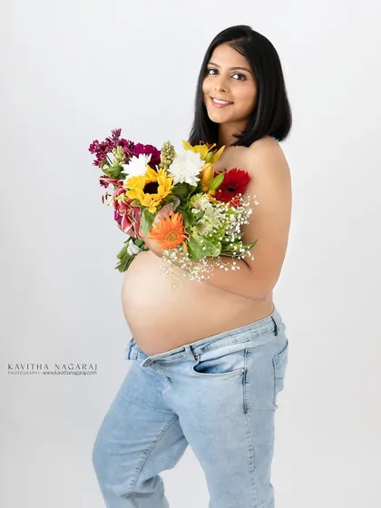A beautiful, minimalist maternity portrait. The mother-to-be holds a bouquet of flowers against her bare belly, creating a fresh and natural look.