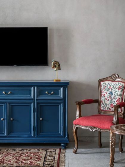 A bold blue console and an ornate, traditionally upholstered chair add a touch of eclectic charm and color to the living space.