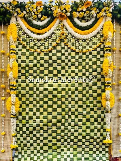 A classic backdrop with a checkerboard pattern of woven leaves. The hanging garlands of marigold and jasmine add a traditional and fragrant element to the decor.