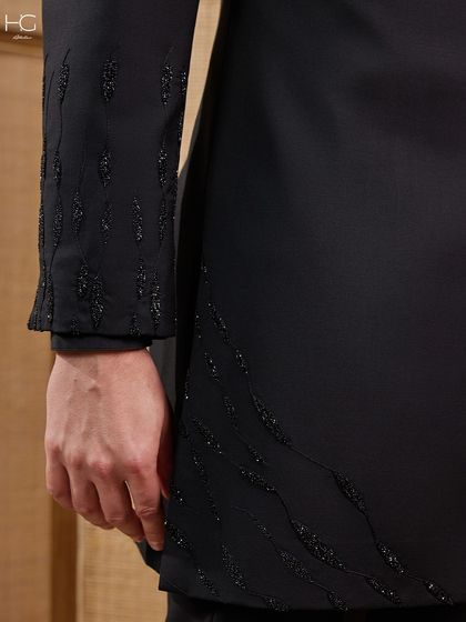 The beauty of this Achkan is in the delicate, cascading embroidery. This detail shot shows the craftsmanship on the sleeve and hem, designed to add a hint of dazzle to the all-black ensemble.