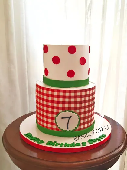 A fun two-tier cake with a red and white gingham pattern on the bottom tier and polka dots on top. A playful design perfect for a pizza party or picnic-themed event.