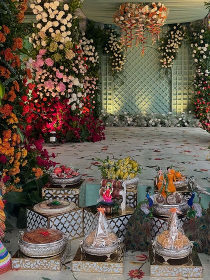 An incredibly lush and colorful floral stage, with massive pillars of flowers in shades of orange, red, pink, and white. The floor is carpeted with petals.