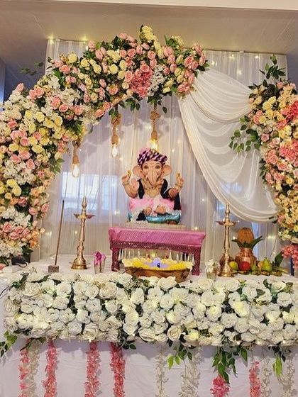 An elegant floral arch in pastel pink and yellow, with soft white drapes in the background. The table is decorated with a border of white flowers and fairy lights, creating a warm and inviting look.