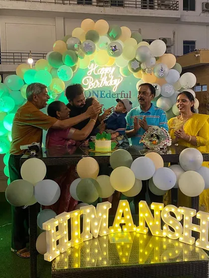 It's all about celebrating with family. This photo shows a 'ONEderful' birthday setup in action, complete with a soft green and yellow balloon arch, a neon sign, and a light-up name sign for the cake-cutting moment.