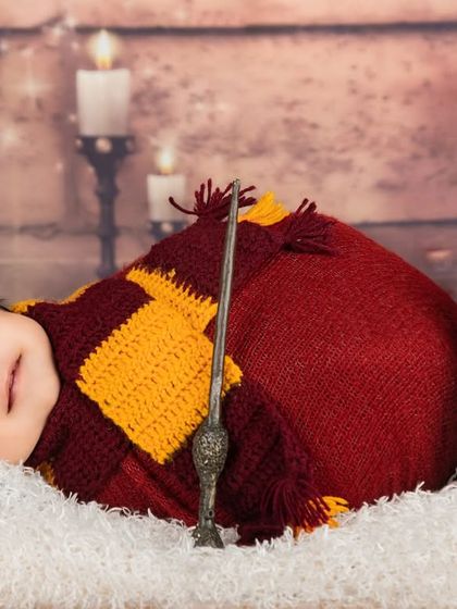 Dreaming of magic. This sleeping newborn is dressed in a Gryffindor-colored wrap, complete with a tiny wand and a knitted owl friend.