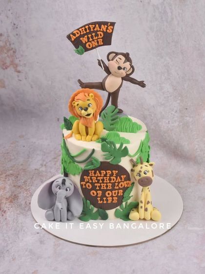 A 'Wild One' jungle-themed cake for a first birthday. This design features cute, friendly animal figurines like a lion, monkey, elephant, and giraffe, perfect for a little explorer's celebration.