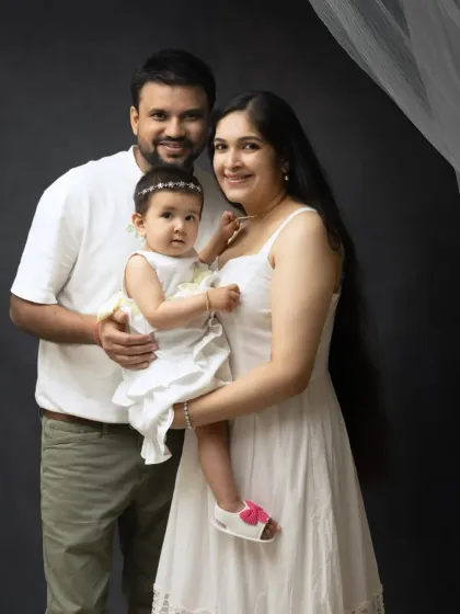 A classic family of three portrait against a dark background. The coordinated white outfits create a clean and cohesive look.