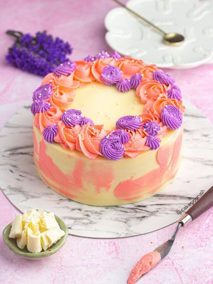 Yes, the perfect birthday cake does exist. This beautiful cake features a pink and yellow marbled buttercream base, topped with delicate pink and purple piped flowers.