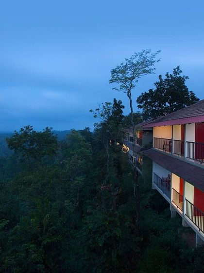 The balconies of Coorg Cliffs Resort at dusk, lit up warmly and offering a stunning, elevated view over the dense forest canopy.