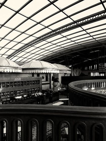 A sweeping black and white shot from the mezzanine, capturing the serpentine curve of the balcony railing as it moves through the space. This highlights the dynamic, multi-level layout.
