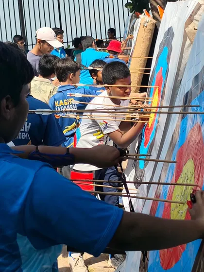 Young archers crowding around the target to score their arrows. The excitement of competition is palpable.