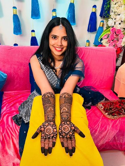 A happy client at her mehndi ceremony, showing off her beautiful floral and peacock design.