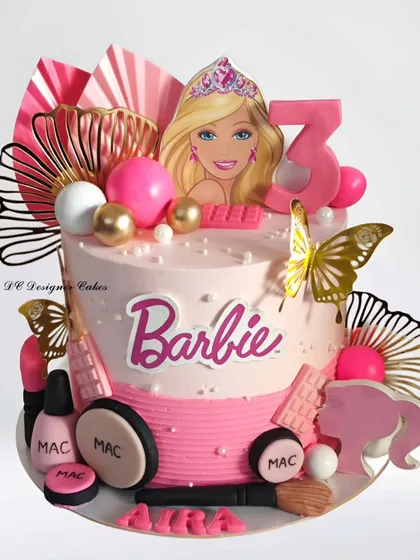 A modern and stylish Barbie cake for a 3rd birthday. This design incorporates trendy elements like paper fans and edible makeup items from MAC, giving it a chic and fashionable look.
