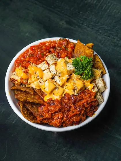 A top-down view of the loaded nacho bowl, showing all the delicious toppings. The dark, moody background helps the colors of the salsa and cheese stand out.