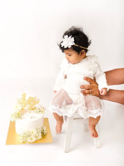 A parent's hands provide support as this six-month-old sits for her half-birthday portrait next to her beautiful cake.