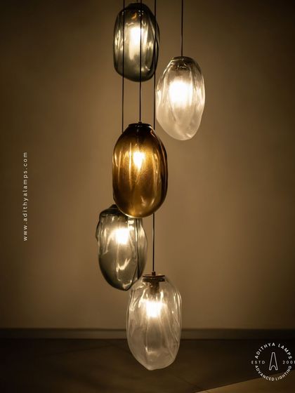 This cascading installation features pendants made of organic, free-form glass in smoked and amber tones. The textured, irregular shapes create a beautiful, water-like effect, perfect for adding a sense of calm and artistry to a room.