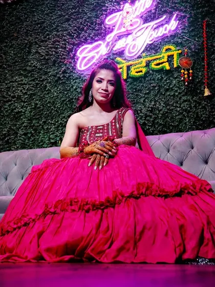 A stunning shot of the bride-to-be on a couch with a "Dulhan ki Mehndi" neon sign. This blends modern decor with traditional celebration.