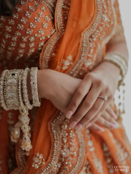 The beauty is in the details. This shot focuses on the bride's hands, adorned with intricate bangles and her wedding ring, resting on the rich fabric of her orange lehenga. It’s these small details that complete the story.