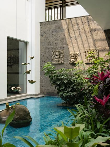 A small, intimate pool surrounded by stone walls and lush planting. The design includes traditional carved stone reliefs and brass bird sculptures, adding layers of art and culture to the water feature.