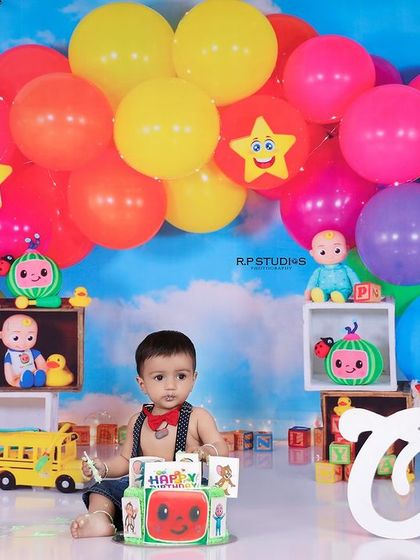 A wide shot of the Cocomelon cake smash setup, with the baby boy sitting happily in the middle. The colorful balloons and props create a vibrant and celebratory mood.