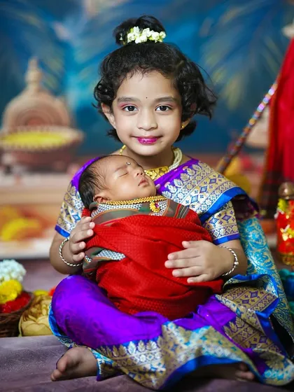 The proud big sister smiles for the camera while cradling her newborn brother, a perfect portrait of sibling love.