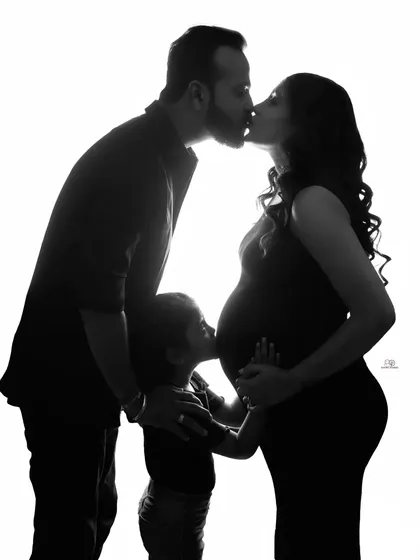 A powerful silhouette capturing a family's love. The parents share a kiss while their son connects with his future sibling, a simple and emotional black and white moment.