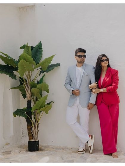 A chic and modern couple portrait against a clean white wall. The contrast between his light suit and her vibrant pink pantsuit creates a stylish and contemporary look.