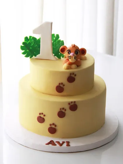 A simple and cute Simba-themed cake for Avi's 1st birthday, featuring the little lion cub and his paw prints.