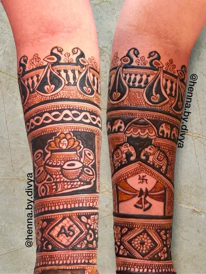 A close-up of the start of a bridal mehendi on the forearms. This design features auspicious symbols like the kalash and swastika, along with peacock and elephant motifs.