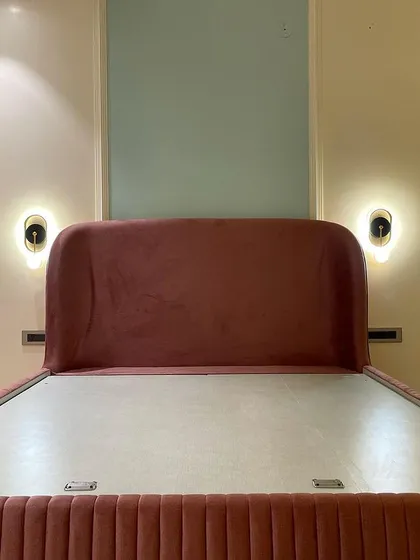 The centerpiece of the 'Rose Room' is this beautiful dusty rose bed. The headboard is flanked by modern wall sconces that provide warm, ambient light, perfect for evening reading.
