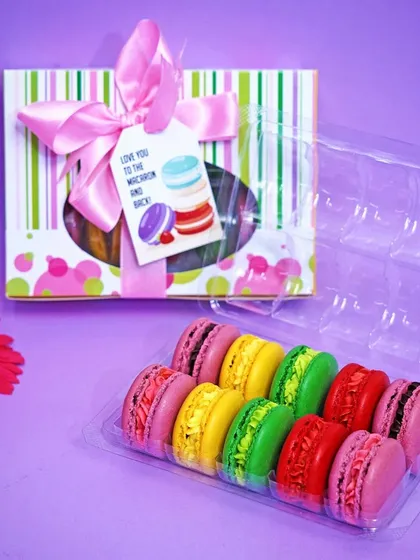 A vibrant display of colorful macarons being placed into a gift box. This image highlights the product's appeal as a perfect gift, focusing on the packaging and presentation.