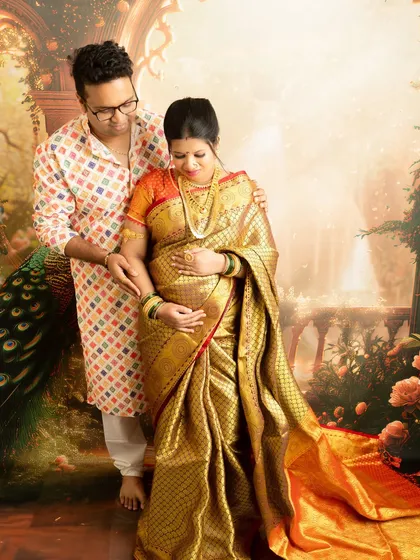 An intimate couple's portrait where the partner gently holds the baby bump. The rich gold of the saree glows under the studio lights.
